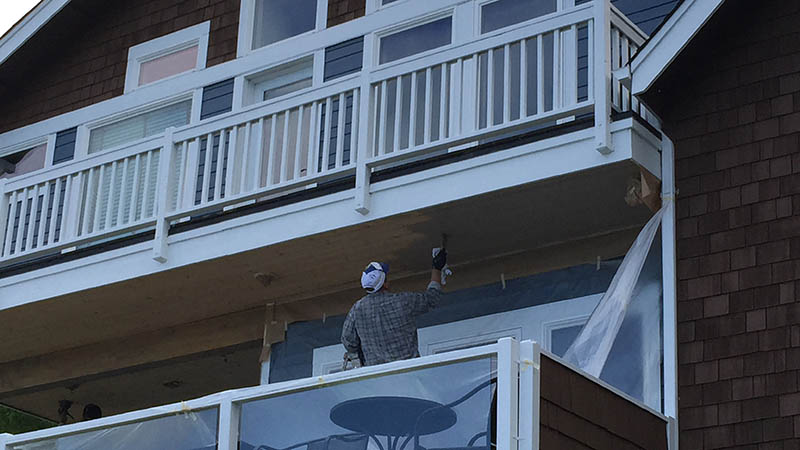 Worker painting underside of house balcony