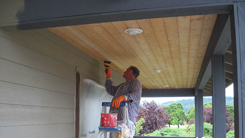 Person painting covered porch ceiling on ladder