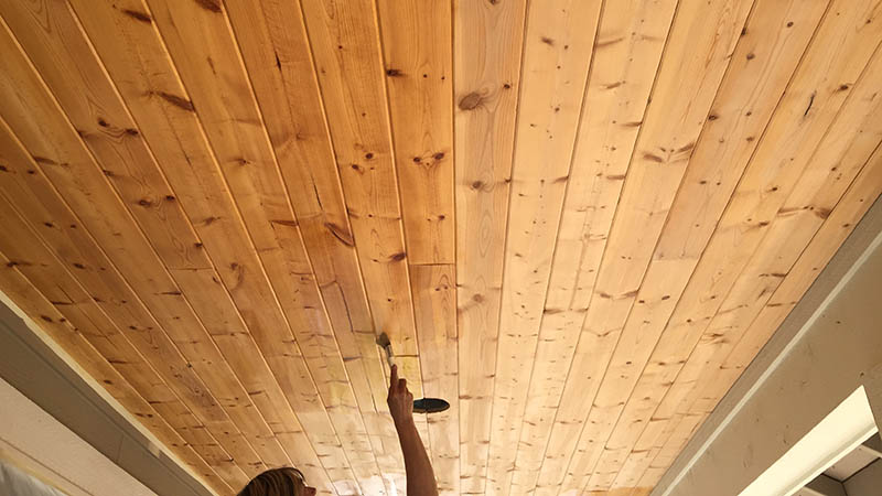 A person brushing the wooden ceiling