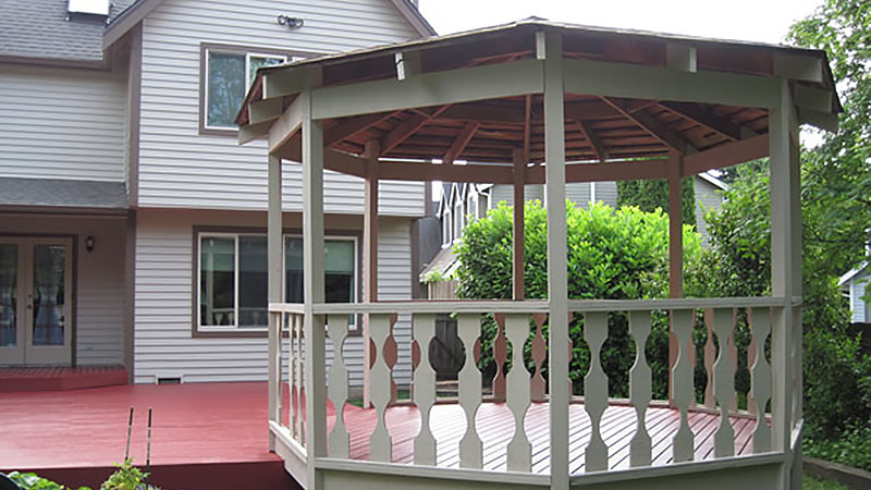 Wooden gazebo on red deck beside house