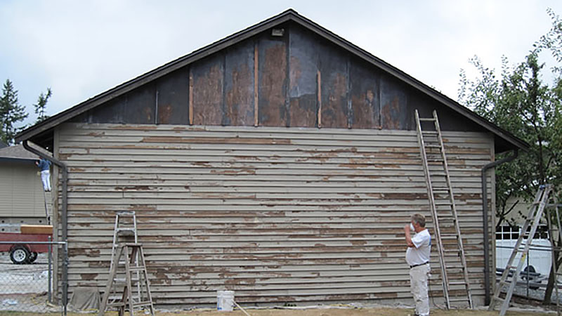 Man inspecting peeling wooden siding with ladders