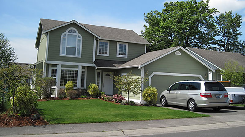Two-story green house with minivan in driveway