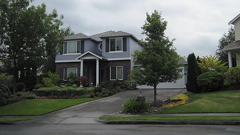 Two-story gray house with driveway and trees