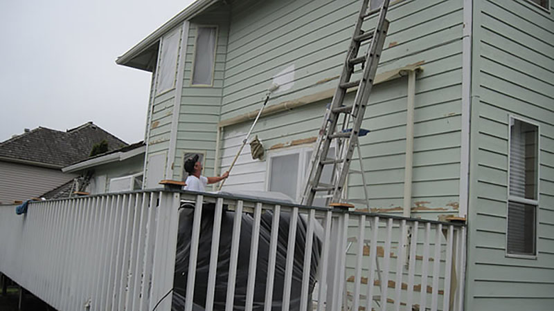 Person painting pale green house exterior