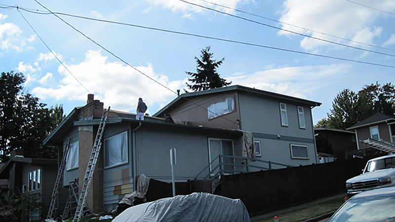 Grey two-story house with roofers and ladders