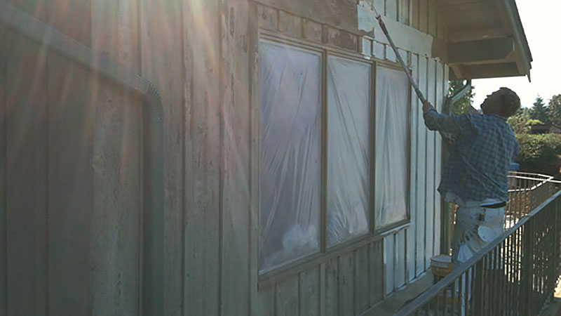 Person painting exterior wooden siding with roller