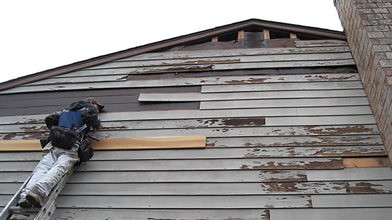 Worker repairing house siding from ladder