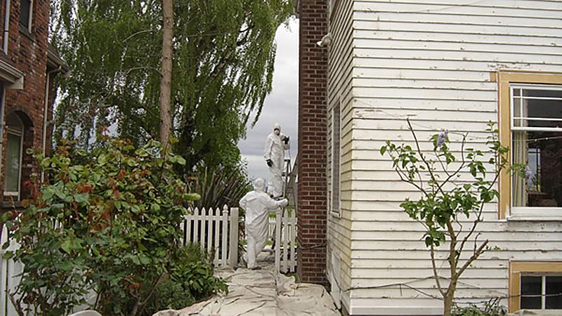 Two workers in white protective suits between houses