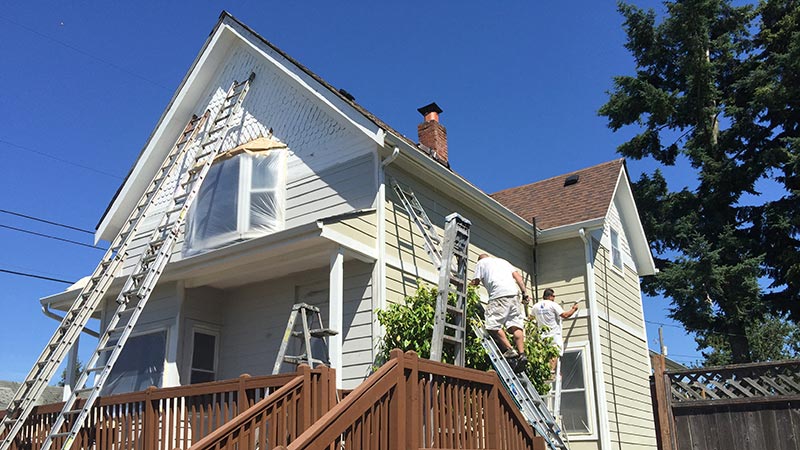 Painters repainting a two-story house with ladders