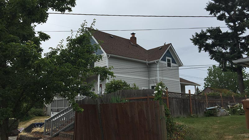Gray two-story house with wooden fence and trees