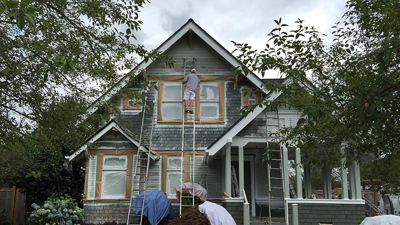 Worker on ladder painting two-story house exterior