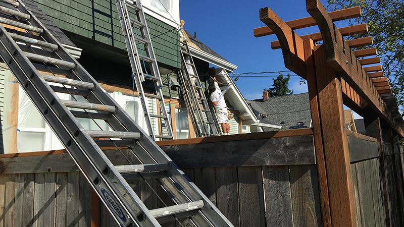 Worker on ladder painting house exterior