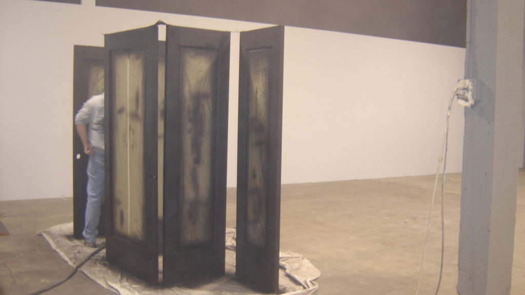 Person spray-painting black doors in empty gallery