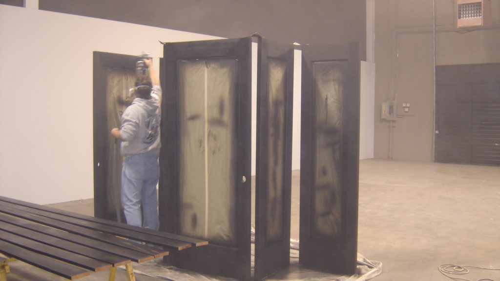 Worker spray-painting large metal doors indoors